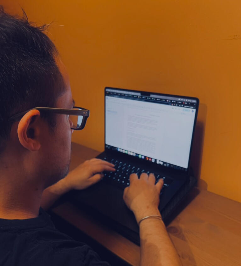 Press Release Creation Image Image of a man from behind, he's typing on a computer with a blurry screen covered in text.