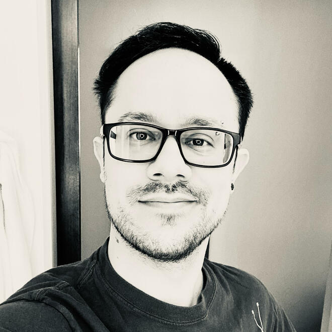 An image in black and white showing a white guy with a closed mouth smile.